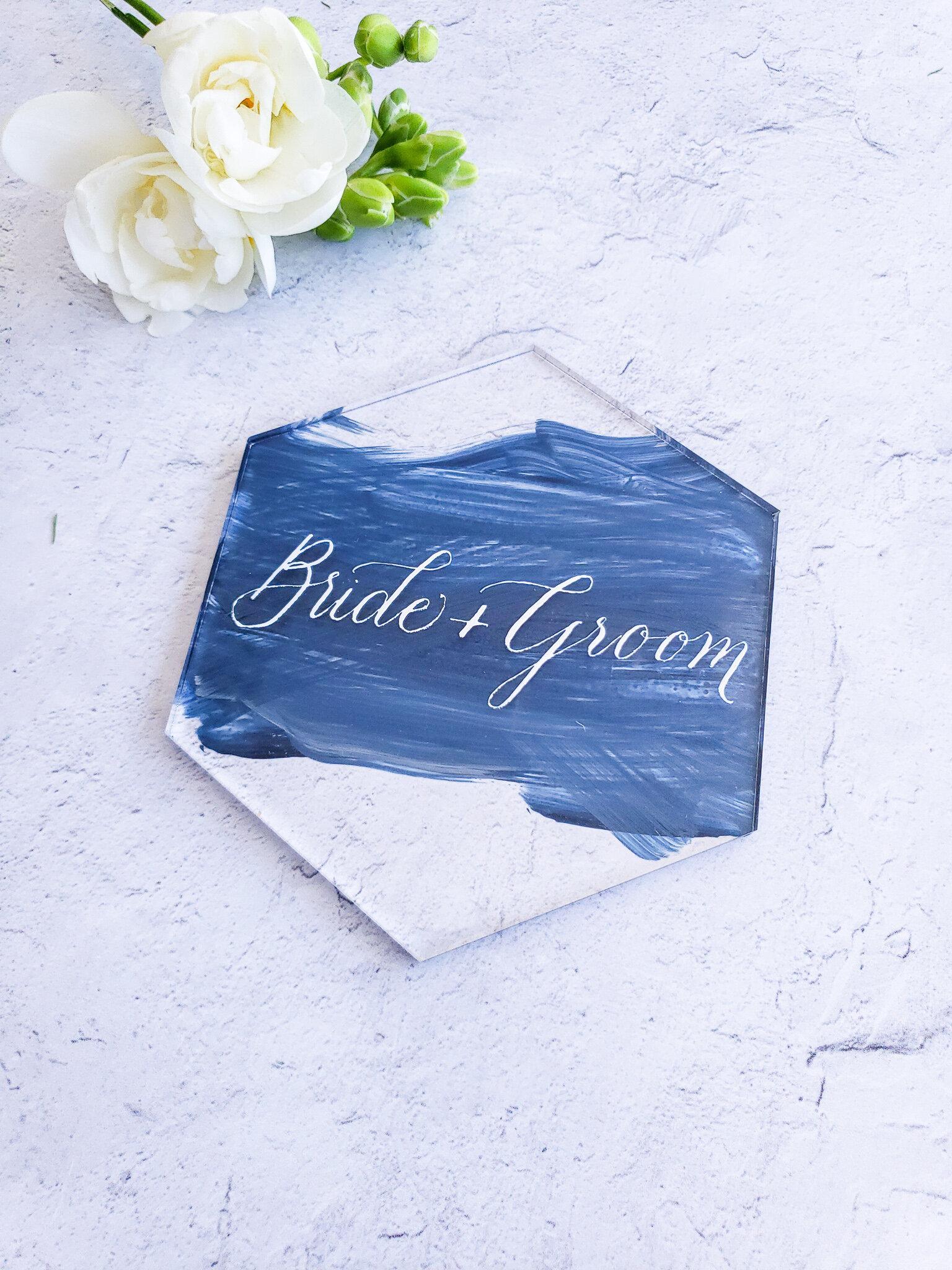 Blue wedding place card with white calligraphy beside greenery