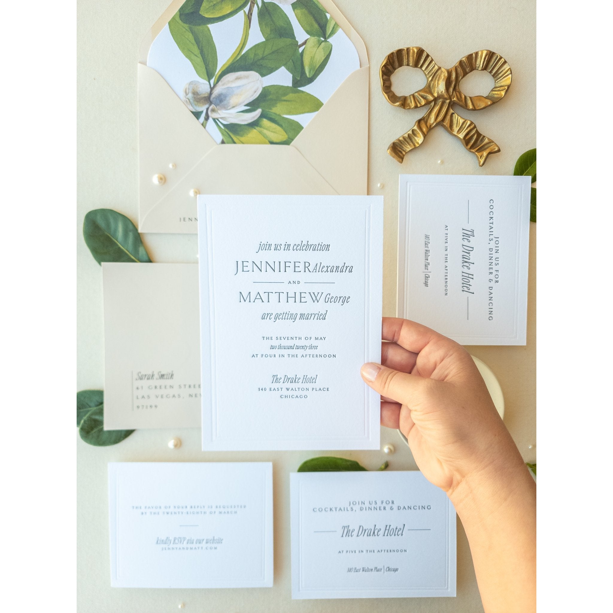 Hand holding a white wedding invitation beside a botanical envelope liner