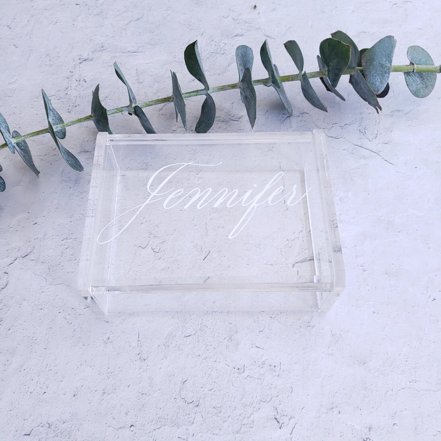 Clear acrylic place card with white calligraphy beside eucalyptus