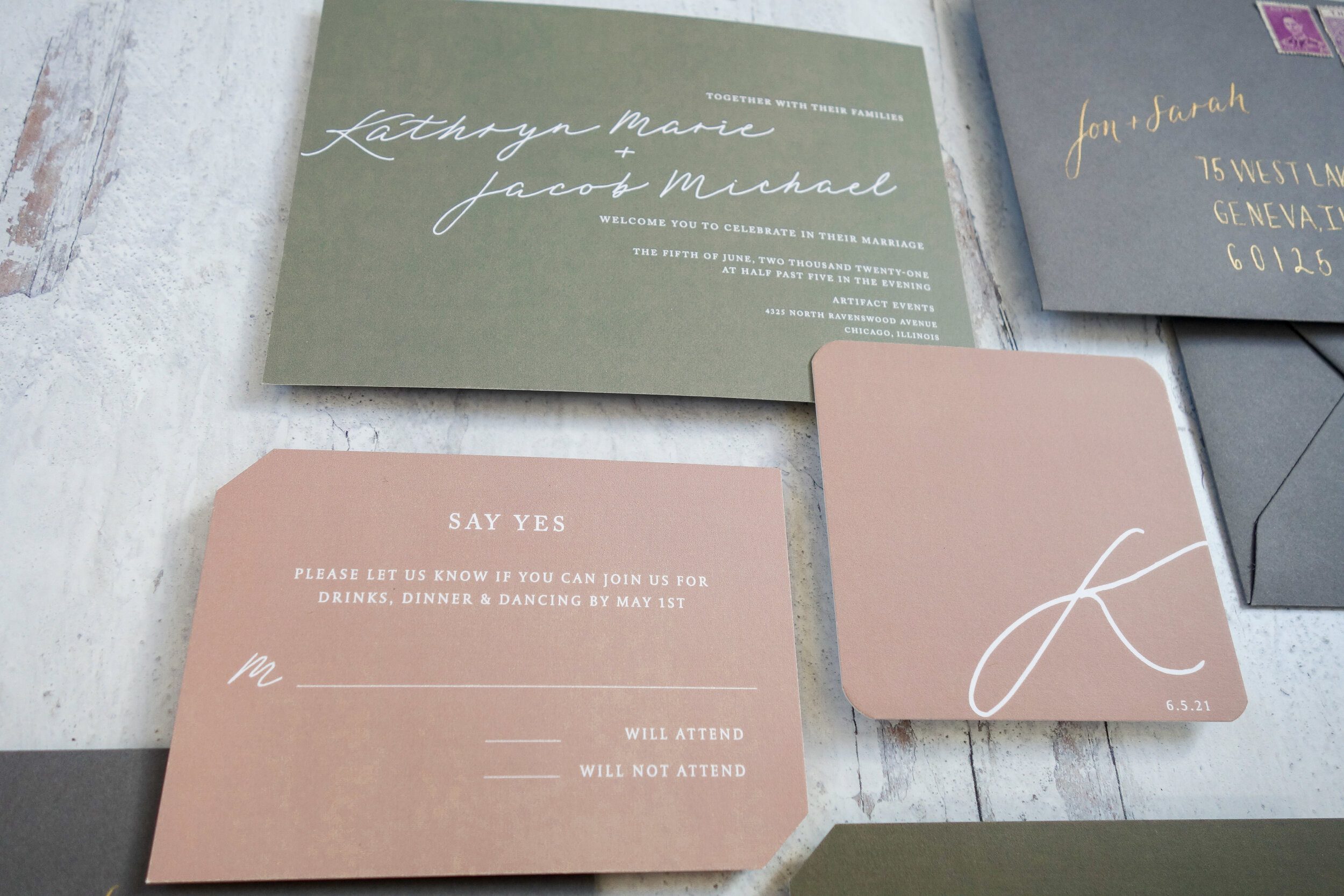 Green invitation with white script beside a gray envelope with gold lettering