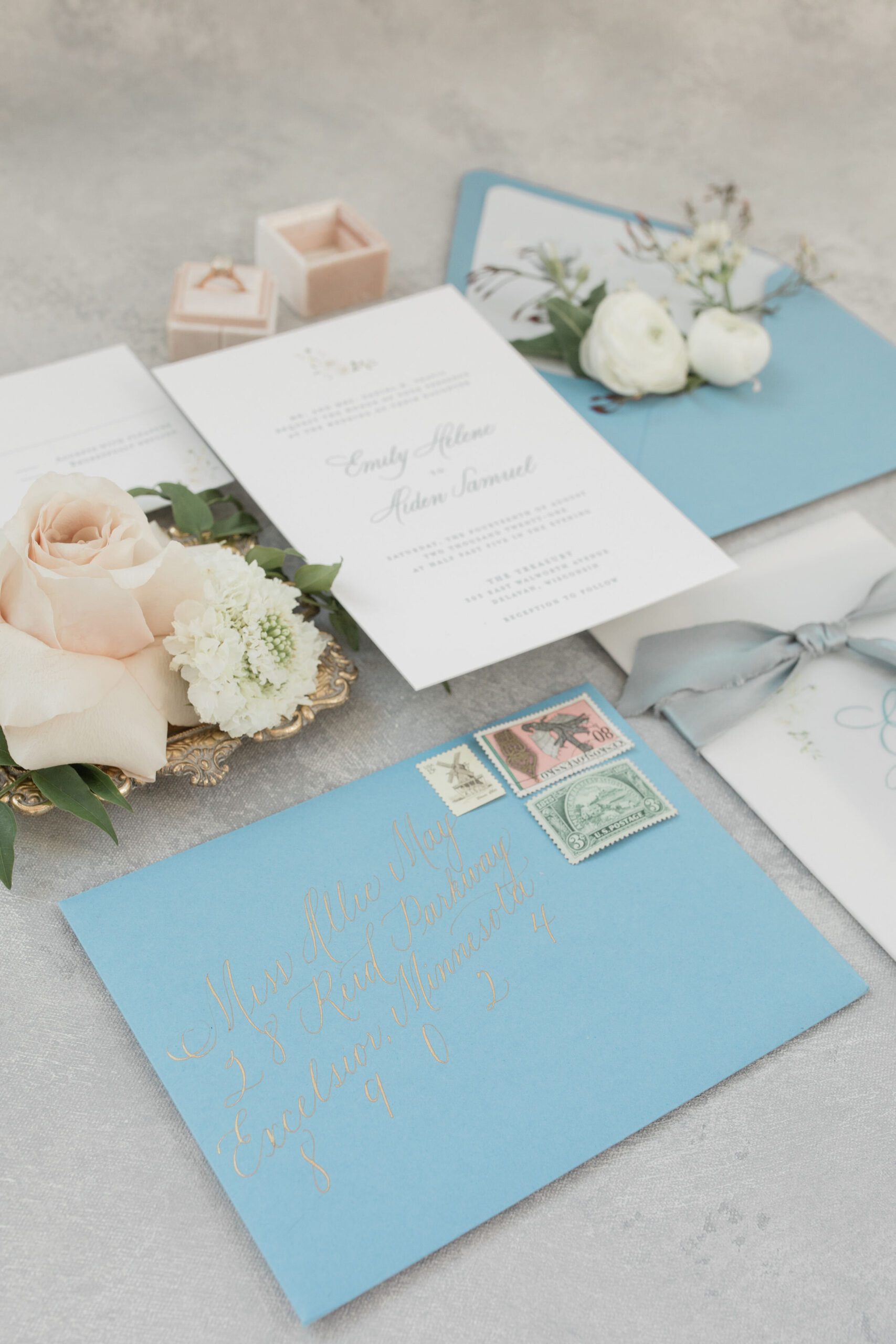 Blue wedding envelope with calligraphy beside a floral invitation suite