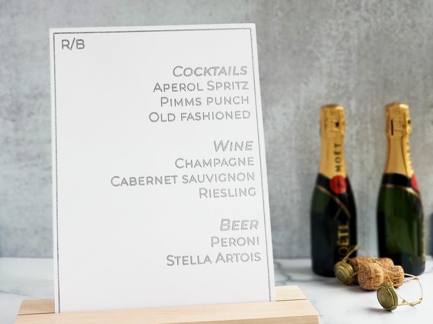 White cocktail and champagne menu sign beside bottles