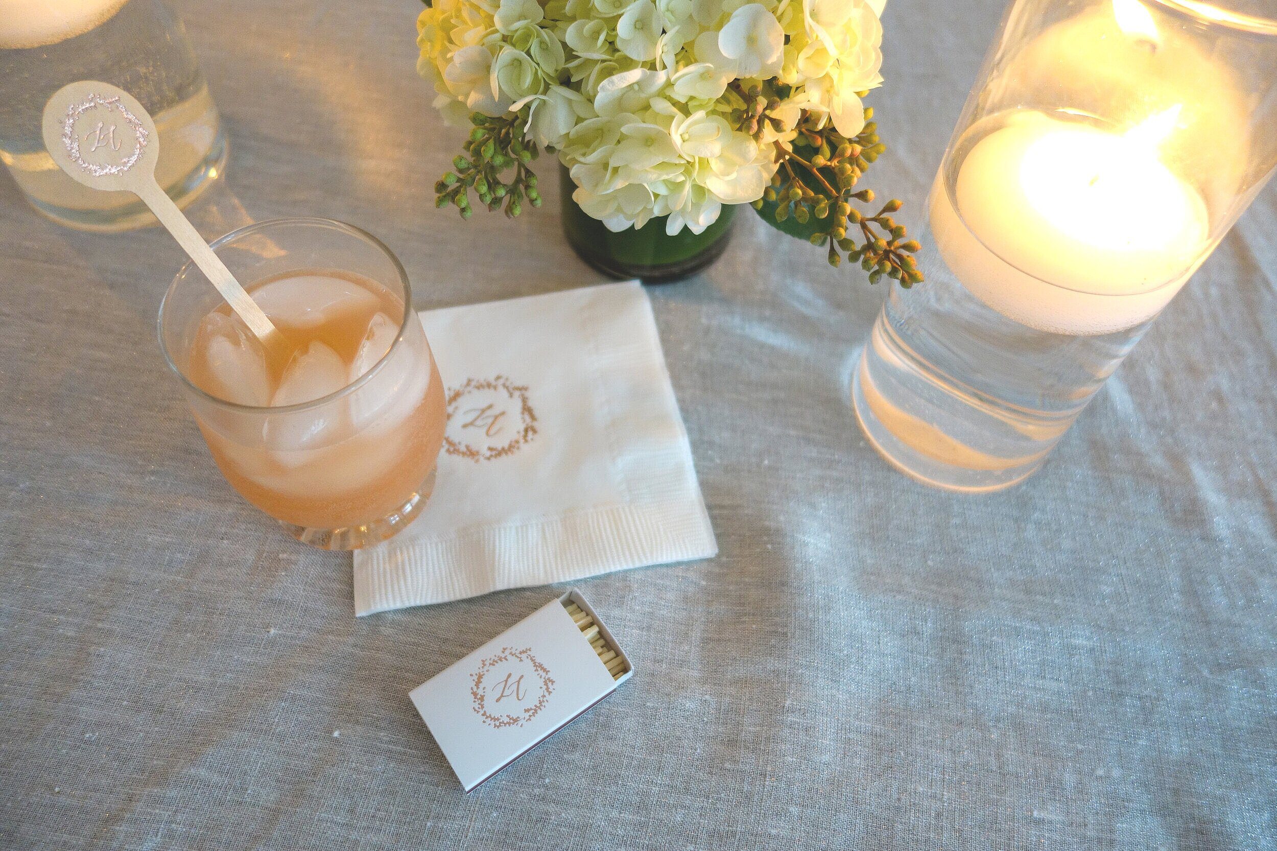 Cocktail napkin and matchbox with a wedding monogram beside a drink