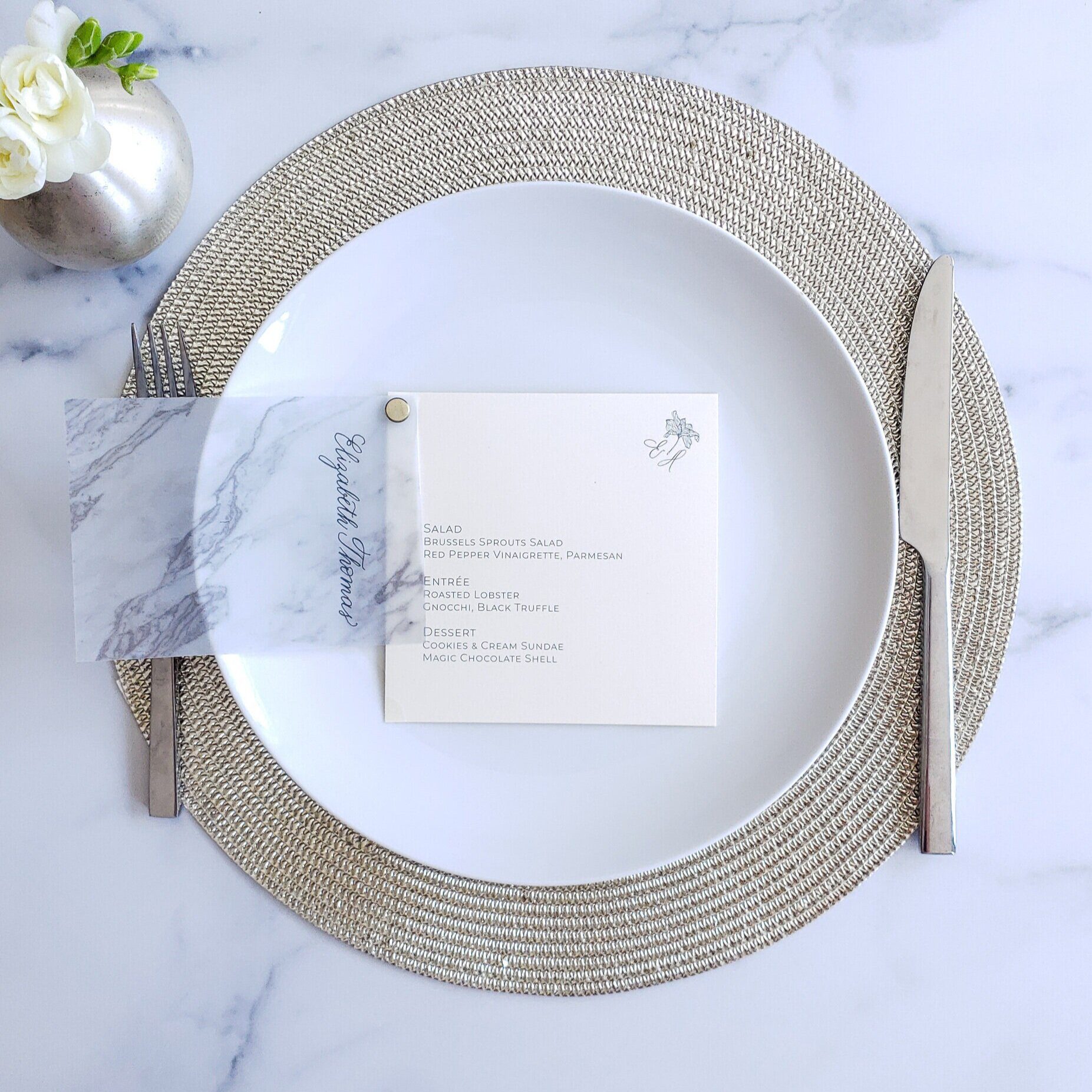 Wedding menu and clear place card on a silver-edged charger